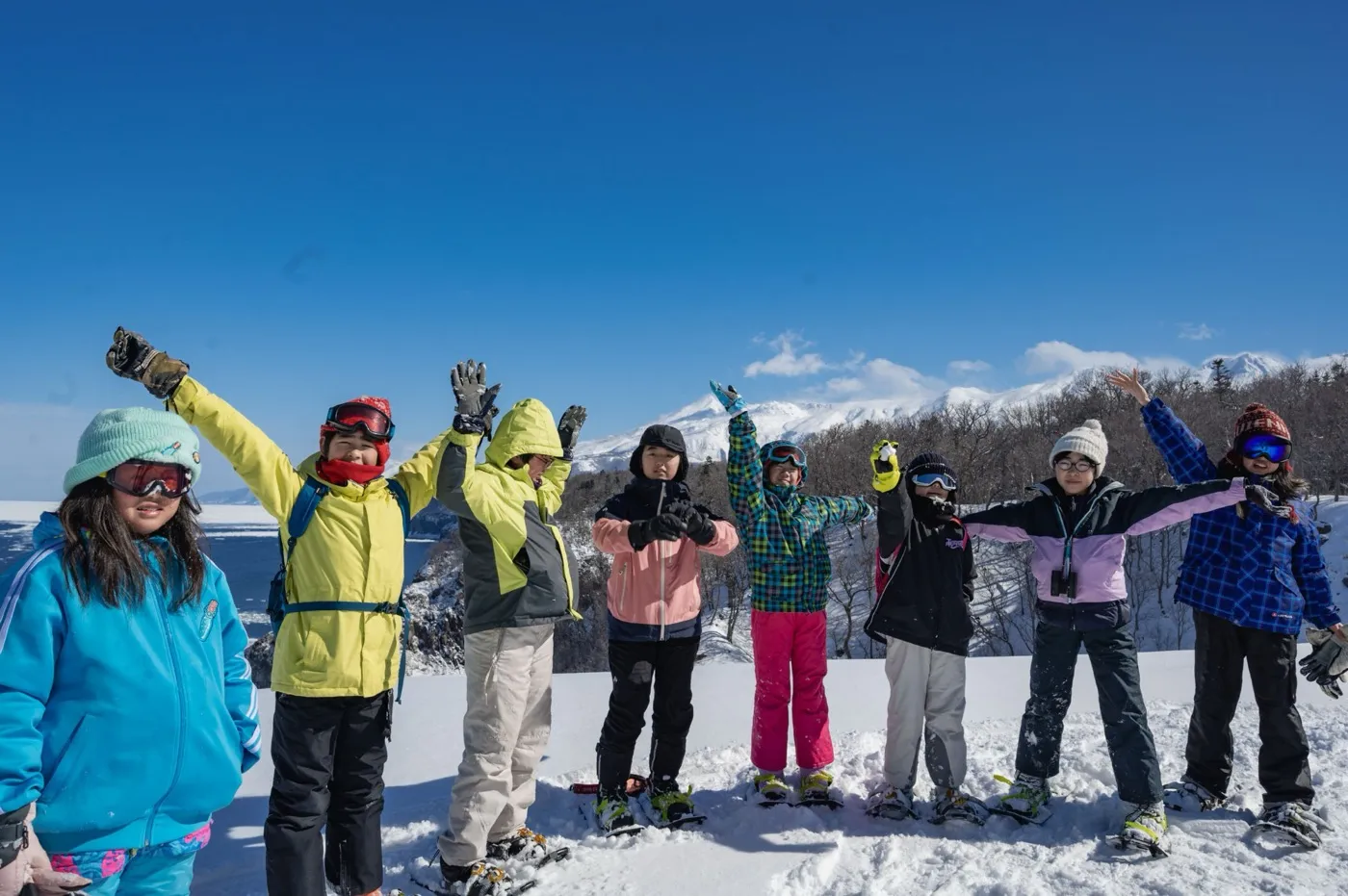 雪山を背に手を挙げる子どもたち